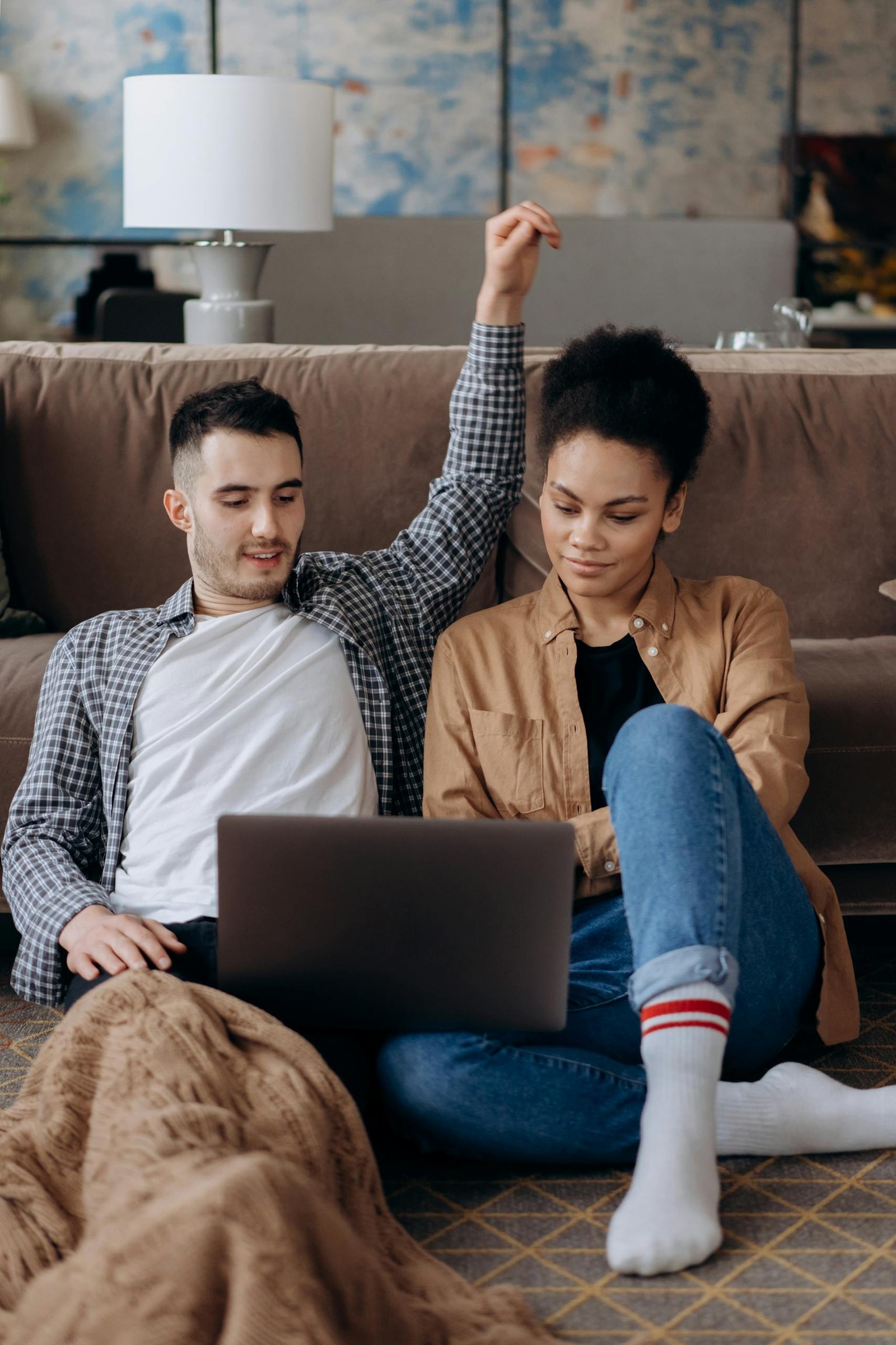 A couple sitting on the floor engaged with a laptop indoors.